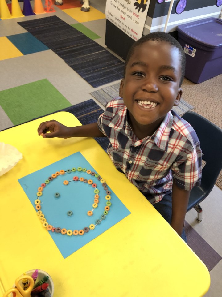 A K4 student makes a smiley face out of cereal.